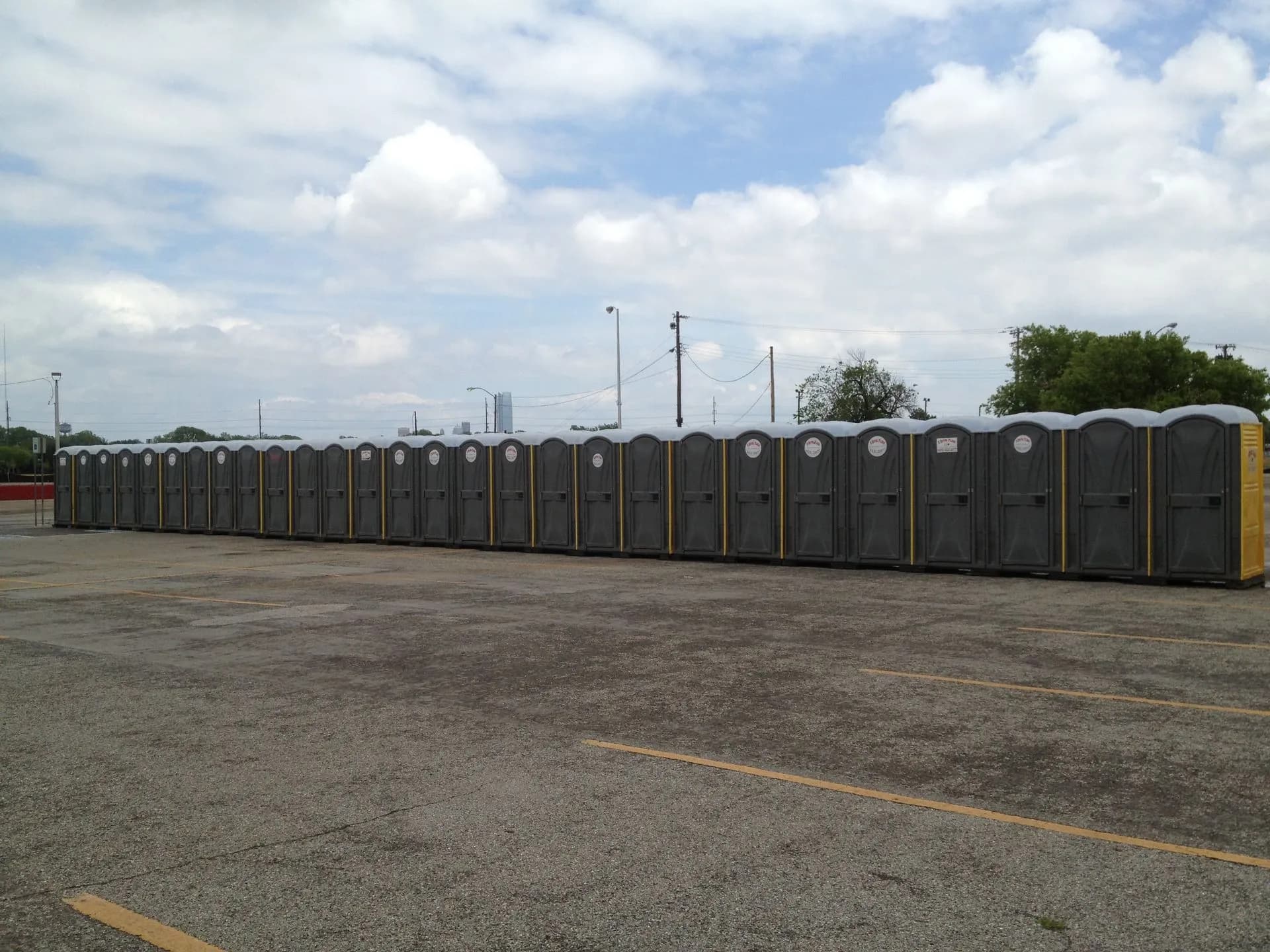 A row of grey portable toilets on a paved construction staging lot