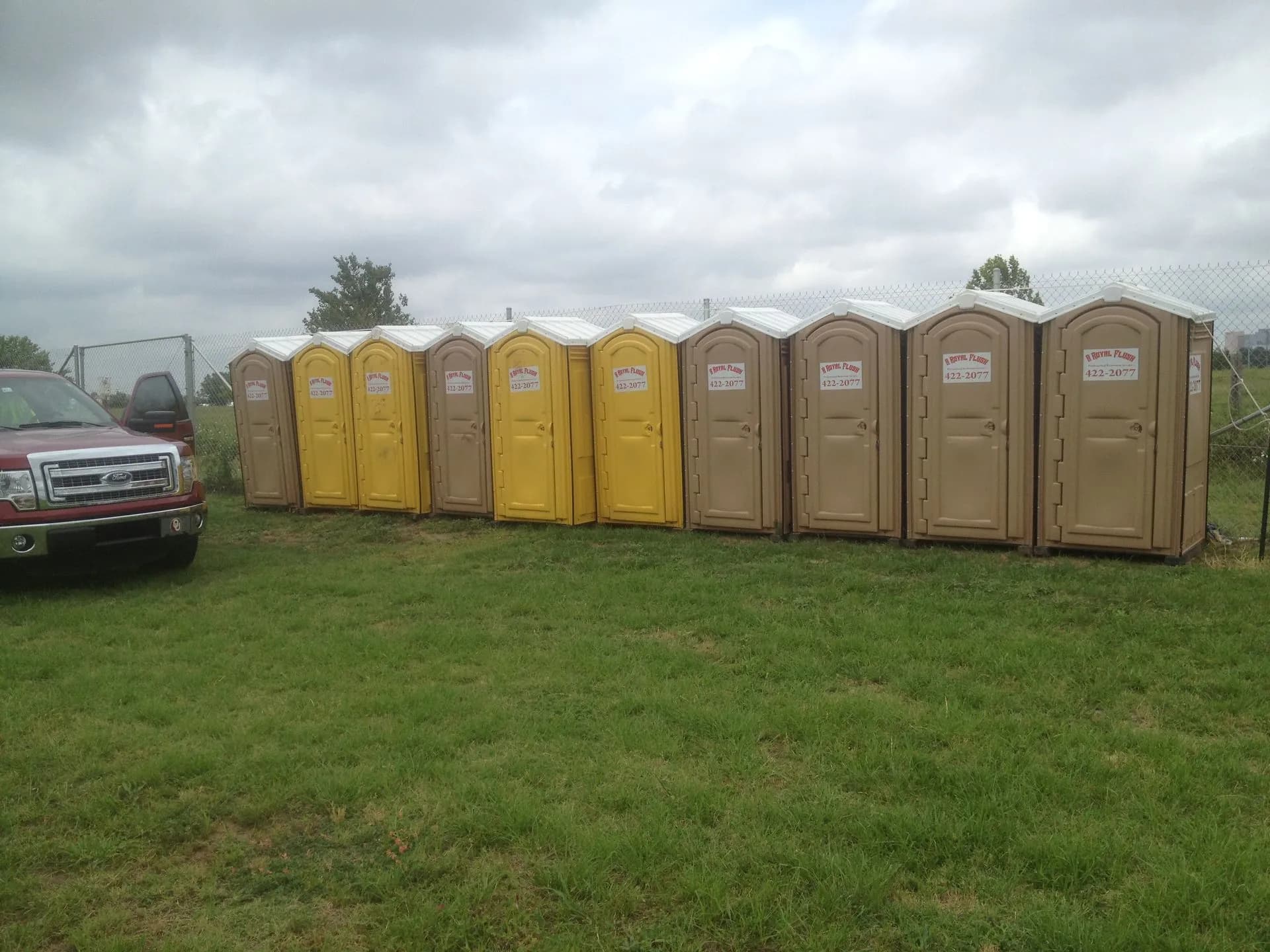 Portable toilets lined up on a work site beside a pickup truck